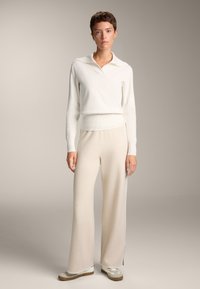 Pulover crem cu guler, asortat cu pantaloni bej cu picioare largi și adidași crem. Textura moale și liniile simple creează un aspect minimalist.