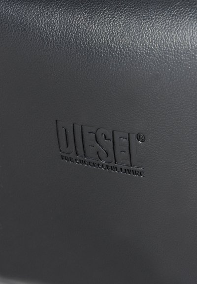 Surface en cuir noir texturé avec logo Diesel embossé et texte "For Successful Living", centrés et légèrement surélevés par rapport au fond.