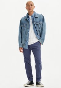 Casaco de ganga em azul claro, T-shirt branca por baixo, calças navy e ténis de cano alto pretos com solas brancas. Conjunto casual, sem padrões.