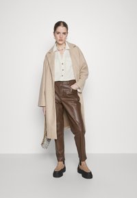 Beige wool coat, light green button-up shirt, brown leather pants, black chunky shoes, and patterned handbag with silver chain strap.