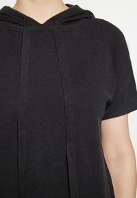 Haut à capuche noir en tissu doux et texturé, avec un col en V, des manches courtes et un cordon de serrage près du cou.
