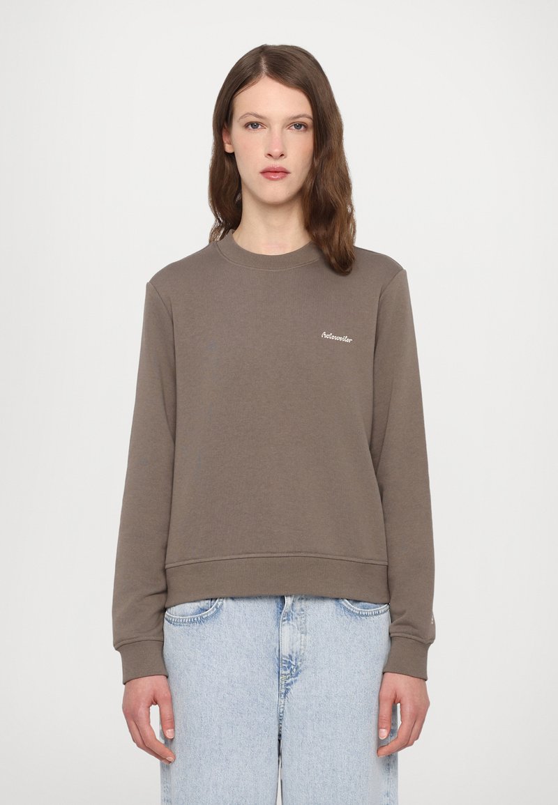 Brun sweatshirt med rund hals, ribbestrikkede mansjetter og kant, med liten brodert logo på brystet. Kombinert med lyseblå jeans.
