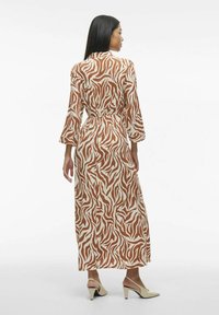 Robe longue à rayures zèbre marron et blanche avec des manches trois-quarts, taille ceinturée, et une silhouette fluide, associée à des talons beiges pointus.