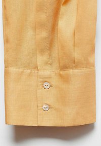 Manschetta di camicia arancione chiaro realizzata in un tessuto liscio, con due bottoni in plastica bianca e dettagli di cucitura ordinati. Presenta una finitura piatta e bordi netti.