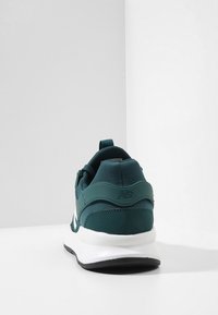 Dark teal sneaker with a textured mesh upper and rubber sole. Features a padded heel and contrasting white midsole. Brand logo on heel.