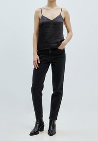 Zwarte satin camisole met verstelbare banden, gecombineerd met donkere high-waisted jeans en zwarte blokhak enkellaarsjes. Eenvoudig en slank ontwerp.