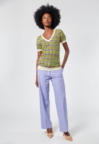 Top de cuello en V y mangas cortas en un patrón de olas verde y amarillo; combinado con pantalones de pierna ancha en un suave color púrpura y tacones de punta beige.