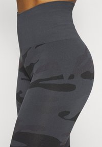 Legginsy z wysokim stanem w ciemnoszarym kolorze z wzorem kamuflażowym. Wykonane z gładkiego, elastycznego materiału z teksturowanym pasem.