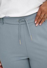 Lys blå bukser med snøring i livet, med sølvfargede detaljer og glatt, elastisk stoff for komfort.