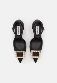 Décolleté nere a punta con cinturino alla caviglia, caratterizzate da una grande fibbia decorata con cristalli sul davanti. Texture in pelle liscia, design elegante.