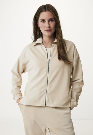 Giacca beige con zip realizzata in tessuto morbido, con collo rialzato e vestibilità comoda. Superficie texturizzata con polsini e orlo a costine.