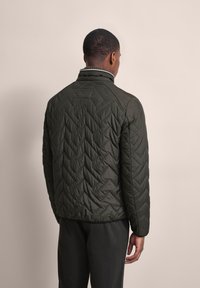 Dark green quilted jacket with a stand collar, featuring a chevron pattern and a fitted cut. Smooth texture and subtle stitching details.