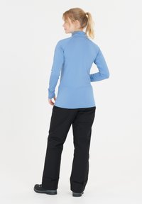 Hellblaues Langarmoberteil mit hohem Kragen, kombiniert mit schwarzen Hosen. Das Outfit hat eine glatte Textur und eignet sich für Outdoor-Aktivitäten.