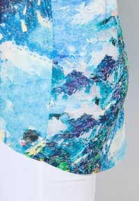 Koszulka z krótkim rękawem z niebieskim abstrakcyjnym wzorem z nutami zieleni, bieli i purpury, wykonana z lekkiego materiału, zestawiona z białymi spodniami.