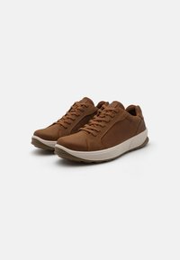 Sneakers din piele maro cu talpă albă contrastantă, design cu șireturi, vârf rotunjit și accente perforate pe laterale.