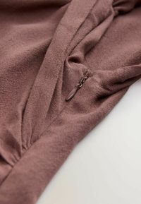 Tessuto morbido di colore malva con una leggera lucentezza, caratterizzato da un dettaglio arricciato e una piccola cerniera con una linguetta in tinta al cucitura.