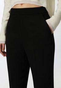 Svarta byxor med en snygg design, slätt tyg, hög midja, sidofickor och en skräddarsydd passform för ett polerat utseende.