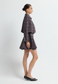 Chaqueta corta de mezcla de lana con patrón geométrico en marrón y azul, combinada con una falda mini acampanada; ambos cuentan con botones crema y tacones negros.