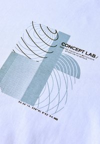 Un tissu blanc présente un imprimé graphique avec des motifs géométriques en bleu clair et gris foncé, comprenant des lignes et des coordonnées, étiqueté "CONCEPT LAB."