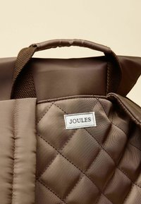 Rjava prešita torba iz blaga z teksturiranimi ročaji. Ponaša se z izrazito oznako "JOULES". Mehki, gladki material s klasičnim dizajnom.