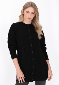Černý pletený cardigan s kulatým výstřihem, vyzna�čující se předními knoflíky a dlouhými rukávy. Texturovaný vzor vytváří vizuální hloubku.