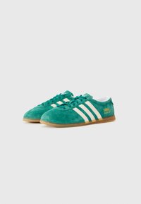 Ténis verdes de camurça com riscas brancas e marca. Biqueira arredondada e design com atacadores, parte superior texturizada e sola de borracha bege.