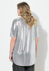 Stříbrný metalický top s krátkým rukávem, zakřiveným lemem a hladkým texturem, mírně volnější střih, spárovaný s tmavými texturovanými kalhotami.