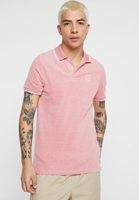 Lyserød polo t-shirt lavet af struktureret stof, med klassisk krave, placket med to knapper og hvid kant ved kraven og ærmerne.