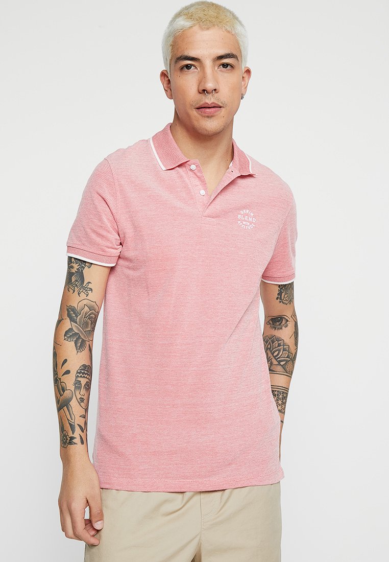 Lyserød polo t-shirt lavet af struktureret stof, med klassisk krave, placket med to knapper og hvid kant ved kraven og ærmerne.