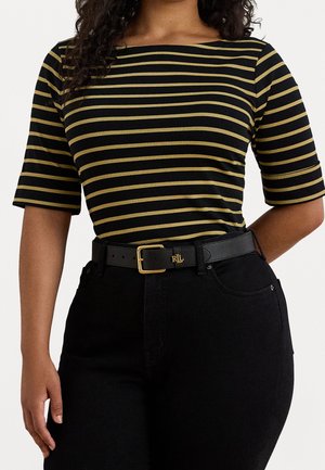 Kvinde iført sort og sennepsstribet kortærmet top, der er stoppet ned i sort højtaljede jeans med sort læderbælte med guldlås.