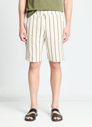 Person wearing cream knit shorts with vertical brown stripes, olive green shirt, and black open-toe sandals, standing on white floor.