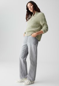 Maglione a coste verde chiaro, fit rilassato, abbinato a jeans grigi chiari a vita alta e sneakers bianche. Design minimalista.