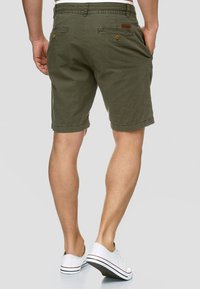 Oliven grønn bomulds shorts med dobbel baglomme, knaplukninger og lige snit, med folded hem og subtil tekstur.