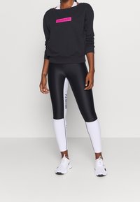 Sweat-shirt noir avec un logo "CALVIN KLEIN" rose, associé à des leggings noir et blanc taille haute avec des inscriptions latérales, et des chaussures blanches.