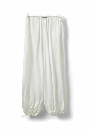 Pantalones blancos de corte holgado con cordones elásticos en la cintura y los tobillos, colgados contra un fondo blanco.