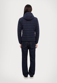 Ναυτική φούτερ τζάκετ με κουκούλα, διαθέτει οριζόντια καπιτονέ τμήματα. Συνδυάζεται με σκούρα τζιν παντελόνια και ανοιχτόχρωμα παπούτσια. Παρουσιάζεται από πίσω.