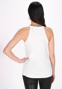 Fehér ujjatlan tank top, kerek nyakkivágással, puha anyagból készült, egyenes aljjal és enyhe oldalsó hasítékokkal a mozgás kényelme érdekében.