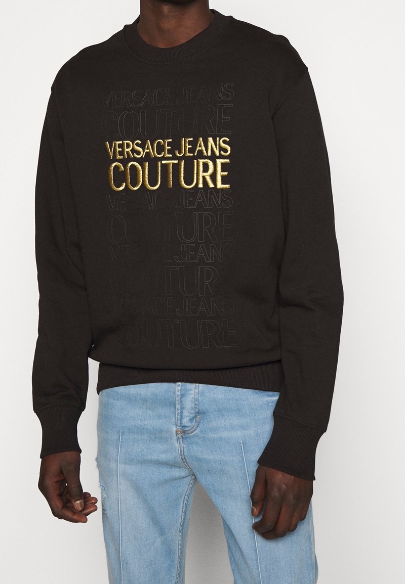 Černá mikina se zešlápnutým vzorem "VERSACE JEANS COUTURE" a zlatě vyšívaným logem. Hladké manžety a lem, měkká látka. Nosit s světle modrými džíny.