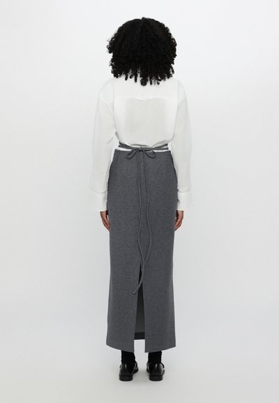 Falda larga gris con una abertura alta, detalle de lazo en la espalda y una textura suave, combinada con una camisa blanca. Diseño sencillo, con detalles mínimos.