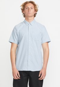 Chemise à manches courtes à boutons en tissu bleu clair, avec une poche, une texture subtile et un design de col classique.