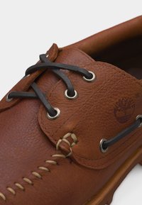 Καφέ δερμάτινο παπούτσι τύπου boat με μαύρα κορδόνια, μεταλλικά ροζέτες, ραφές μοκασίνου και ανάγλυφο λογότυπο δέντρου στο πλάι.