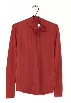 Langærmet bluse i rustfarve med en blød tekstur, der har en sløjfedetalje ved halsen og en rund kant. Fremstillet af letvægtsstof.