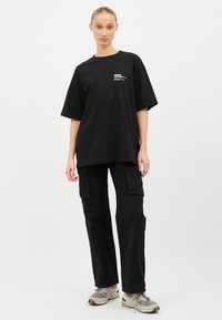 Schwarzes, oversized T-Shirt mit kurzen Ärmeln und einem kleinen Grafikprint, kombiniert mit schwarzen Cargo-Hosen mit seitlichen Taschen und lockerer Passform.