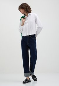 Camicia bianca corta con bottoni, jeans scuri a vita alta con risvolti, e scarpe nere. Design semplice, texture liscia e vestibilità su misura.