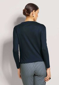 Marineblaue Langarmoberteil mit glatter Textur und abgerundetem Saum, kombiniert mit gemusterten Hosen, die sechseckige Formen in Blau und Weiß zeigen.