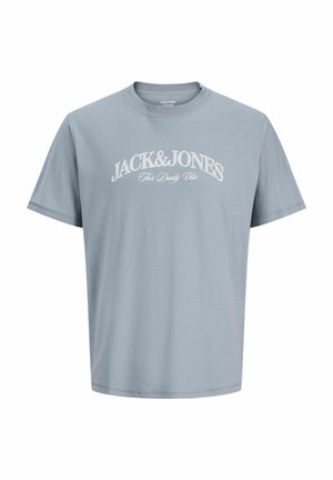 Jongen met kort blond haar die een lichtblauw Jack & Jones t-shirt, beige korte broek, witte sokken en witte sneakers draagt, staand tegen een neutrale achtergrond.
