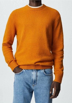 Un pull orange en maille avec un col rond, des manches longues et des poignets côtelés. Associé à un jean en denim bleu clair, mettant en valeur une tenue décontractée.