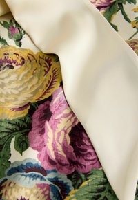 Tessuto floreale con grandi motivi di rose gialle, rosa e verdi, abbinato a un elegante bordo in raso di colore crema.