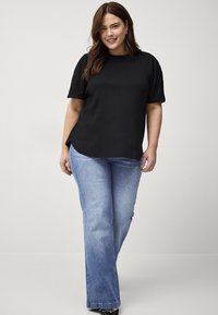 Zwart, gestructureerd, kort mouwtop gecombineerd met lichtblauwe flared jeans. Het topje heeft een ronde halslijn en een ontspannen pasvorm.