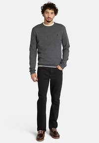 Harmaa neulepaita, jossa on pyöreä pääntie, pitkät hihat ja resorit hihansuissa, yhdistetty mustiin farkkuihin ja ruskeisiin nauhakenkäisiin. Yksinkertainen malli, ilman kuoseja.